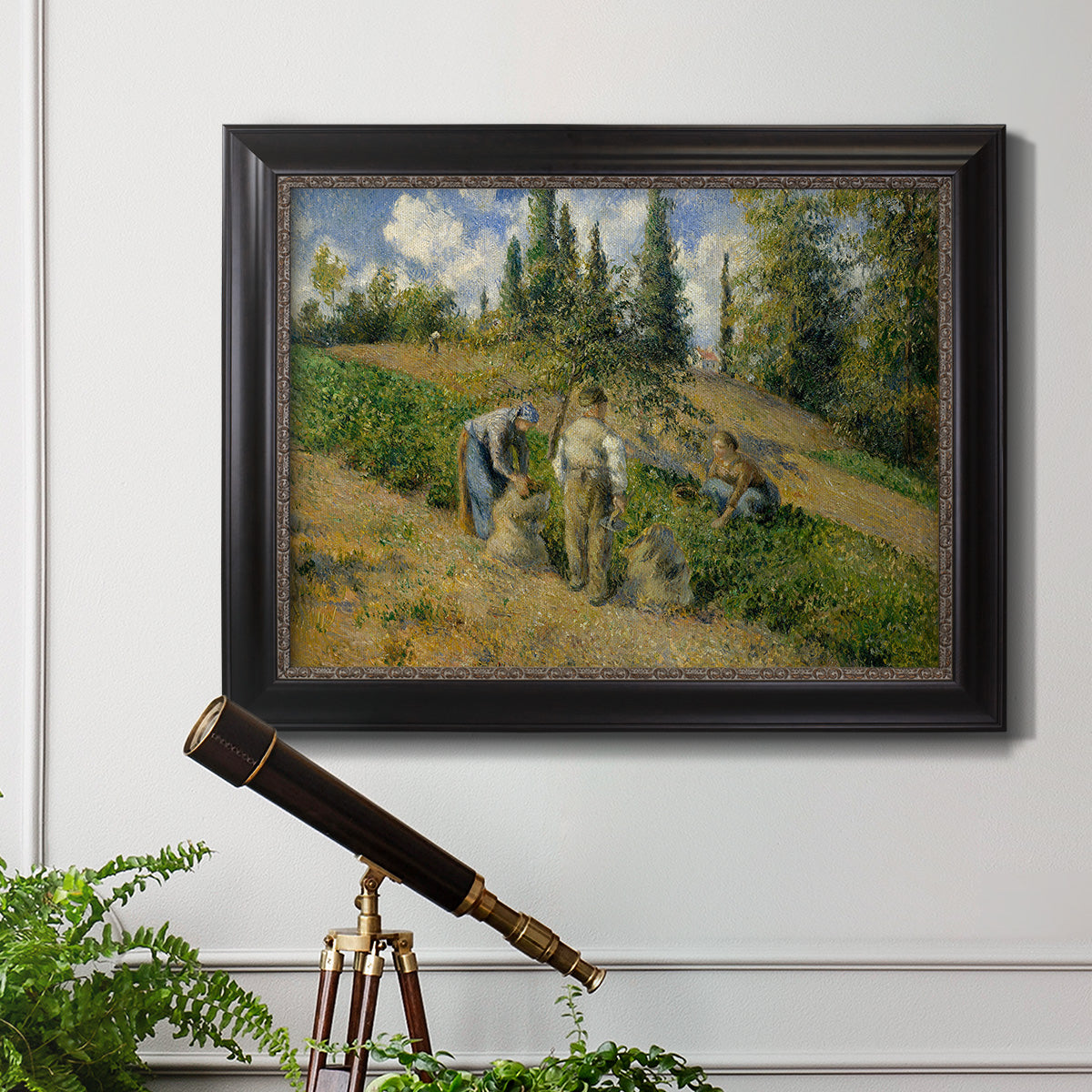Impressionist countryside harvest scene by Camille Pissarro in an ornate black frame with gilded inner detail displayed in a light-toned interior setting.