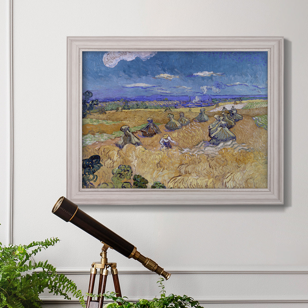 Impressionist wheat harvest scene by Vincent van Gogh in an ornate weathered white frame displayed in a light-toned interior setting.