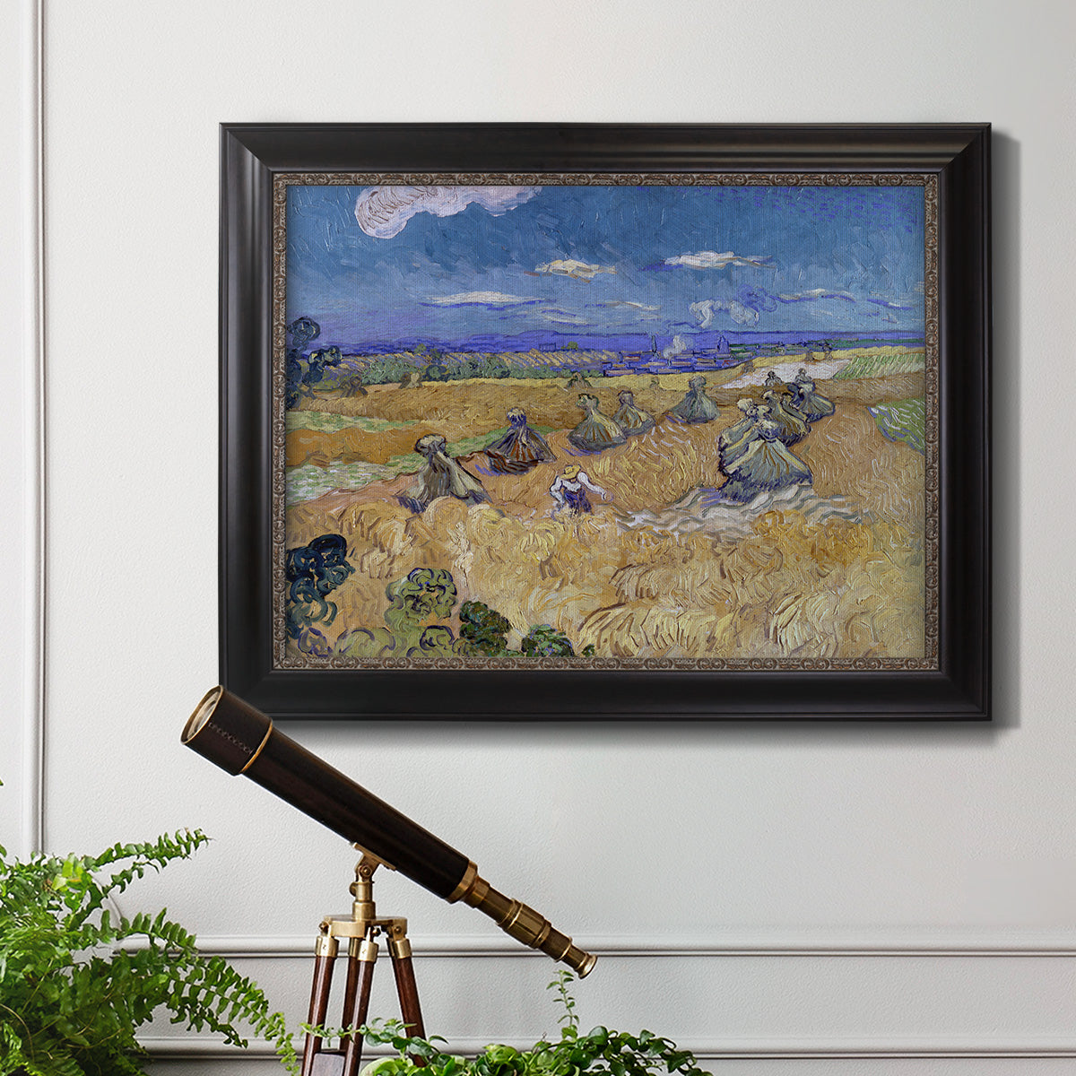 Impressionist wheat harvest scene by Vincent van Gogh in an ornate black frame with gilded inner detail displayed in a light-toned interior setting.
