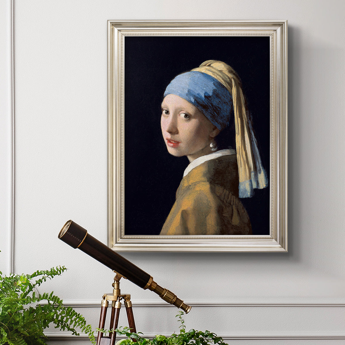 Iconic portrait of a girl wearing a pearl earring by Johannes Vermeer in an ornate champagne frame displayed in a light-toned interior setting.
