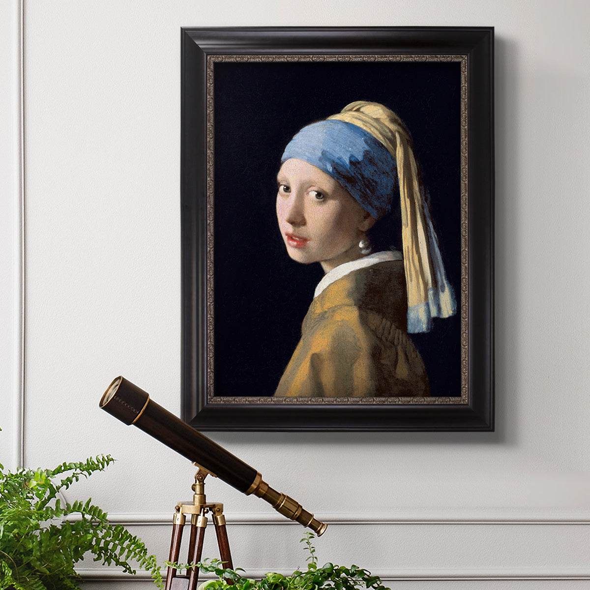 Iconic portrait of a girl wearing a pearl earring by Johannes Vermeer in an ornate black frame with gilded inner detail displayed in a light-toned interior setting.