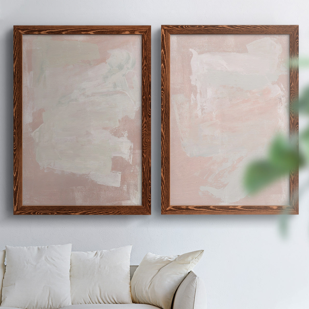 Set of two maple barnwood framed canvas prints depicting cloudy rose washes, broad pale strokes, and subtle texture arranged across two complementary compositions above a sofa in a bright living space.