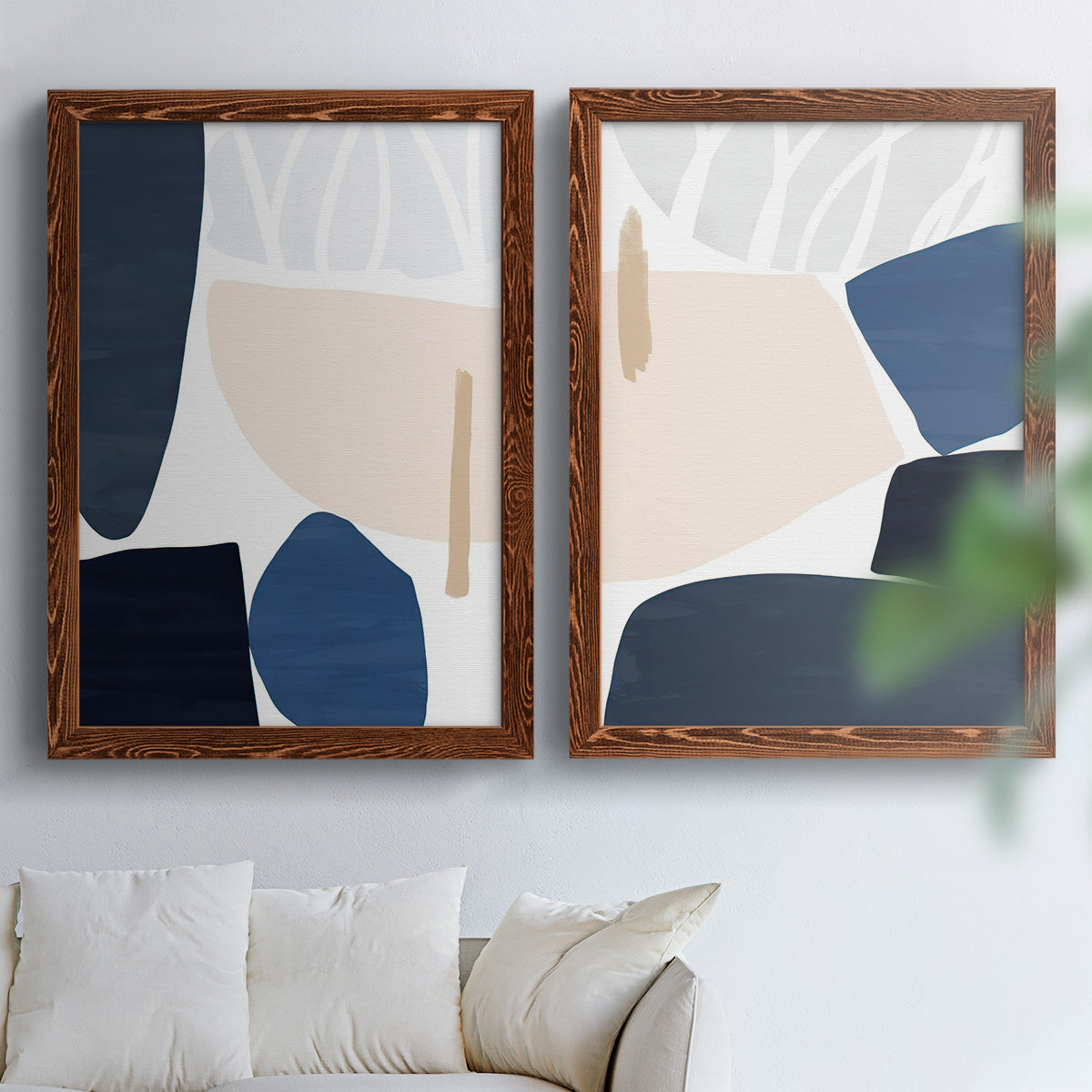 Set of two maple barnwood framed canvas prints depicting rounded dark forms, pale sand fields, and clean modern edges arranged across two complementary compositions above a sofa in a bright living space.