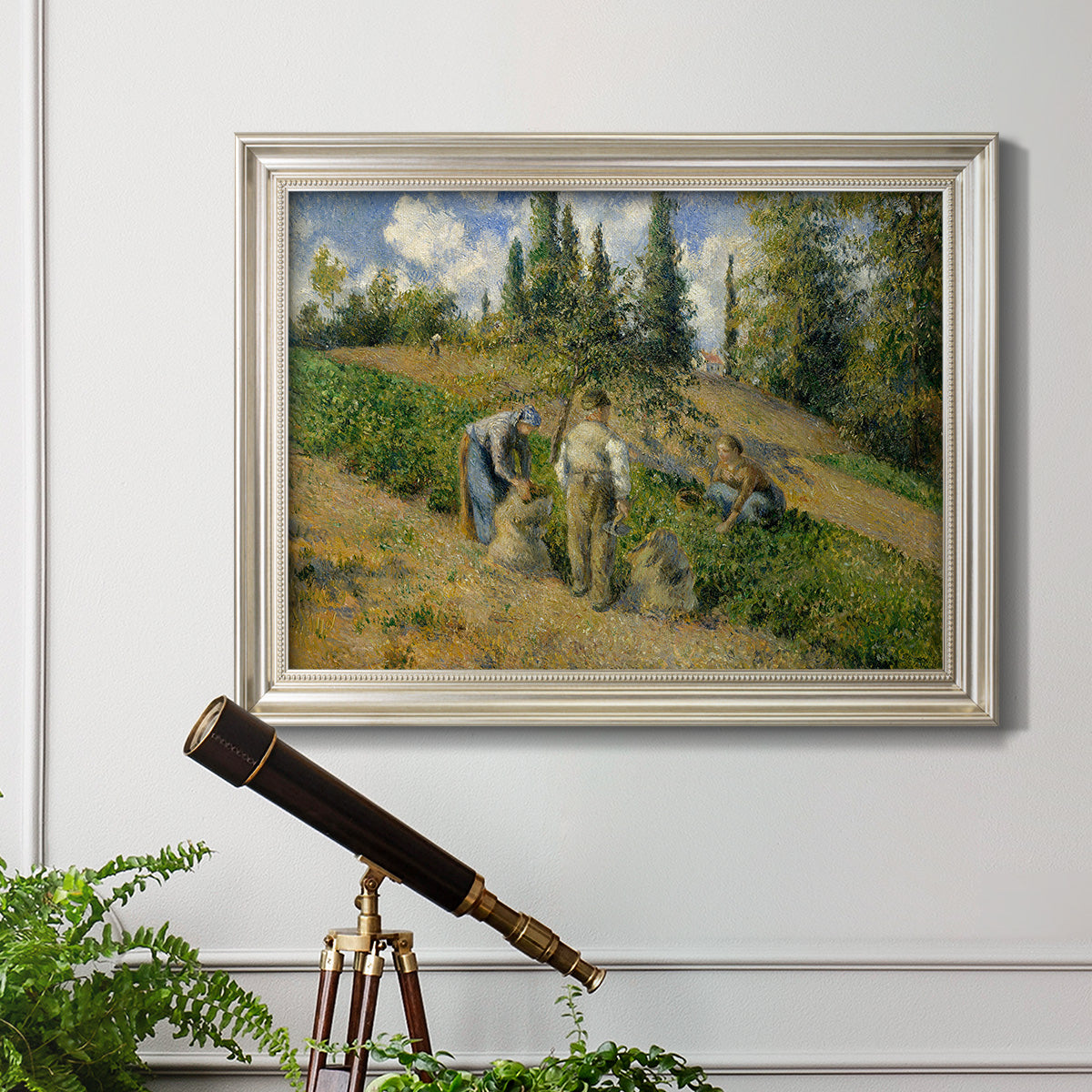 Impressionist countryside harvest scene by Camille Pissarro in an ornate champagne frame displayed in a light-toned interior setting.