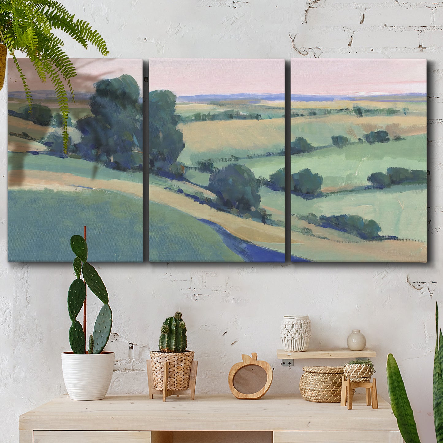 Three-panel canvas wall art featuring pastoral countryside with rocky outcrop, displayed in a boho-chic entryway above a console table.