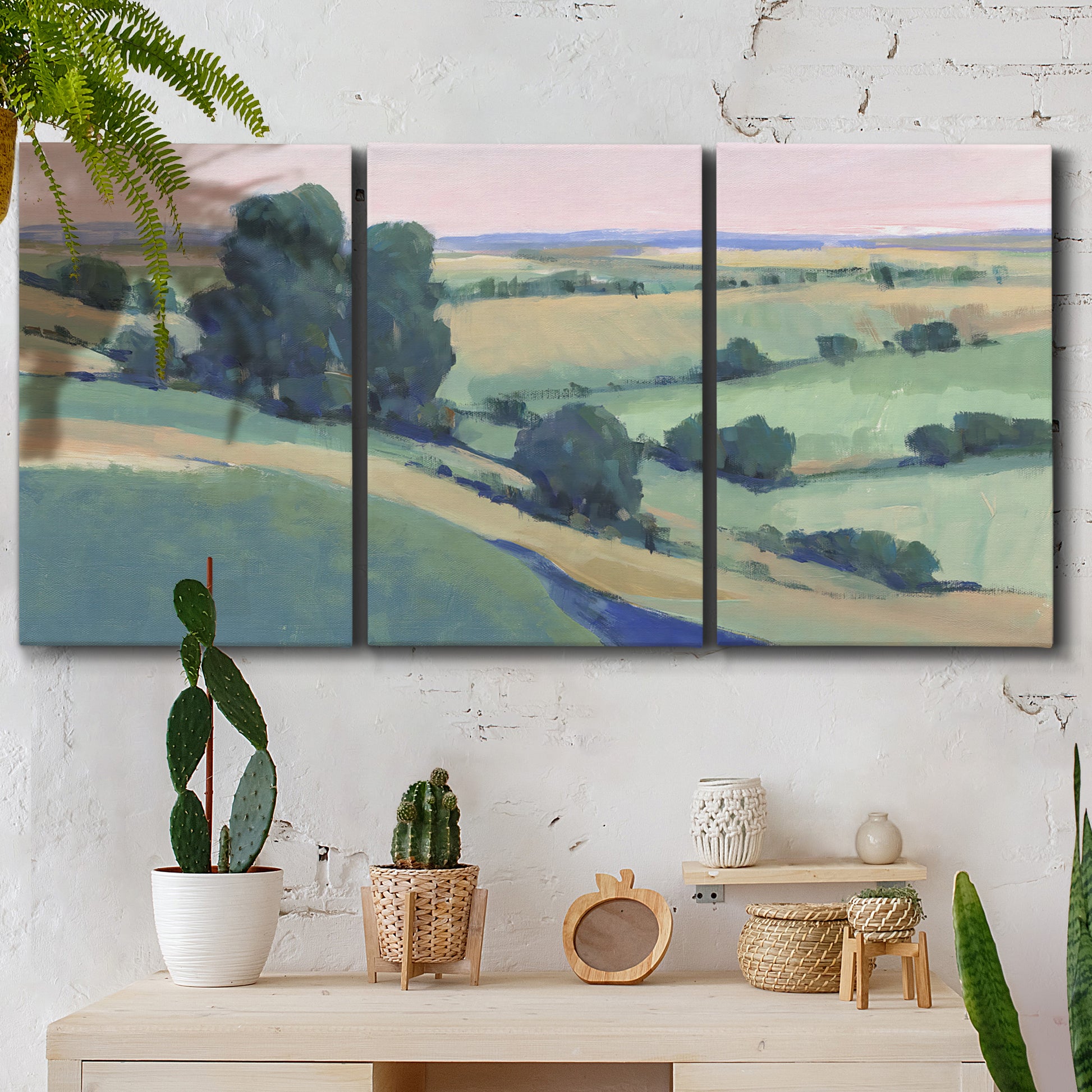 Three-panel canvas wall art featuring pastoral countryside with rocky outcrop, displayed in a boho-chic entryway above a console table.