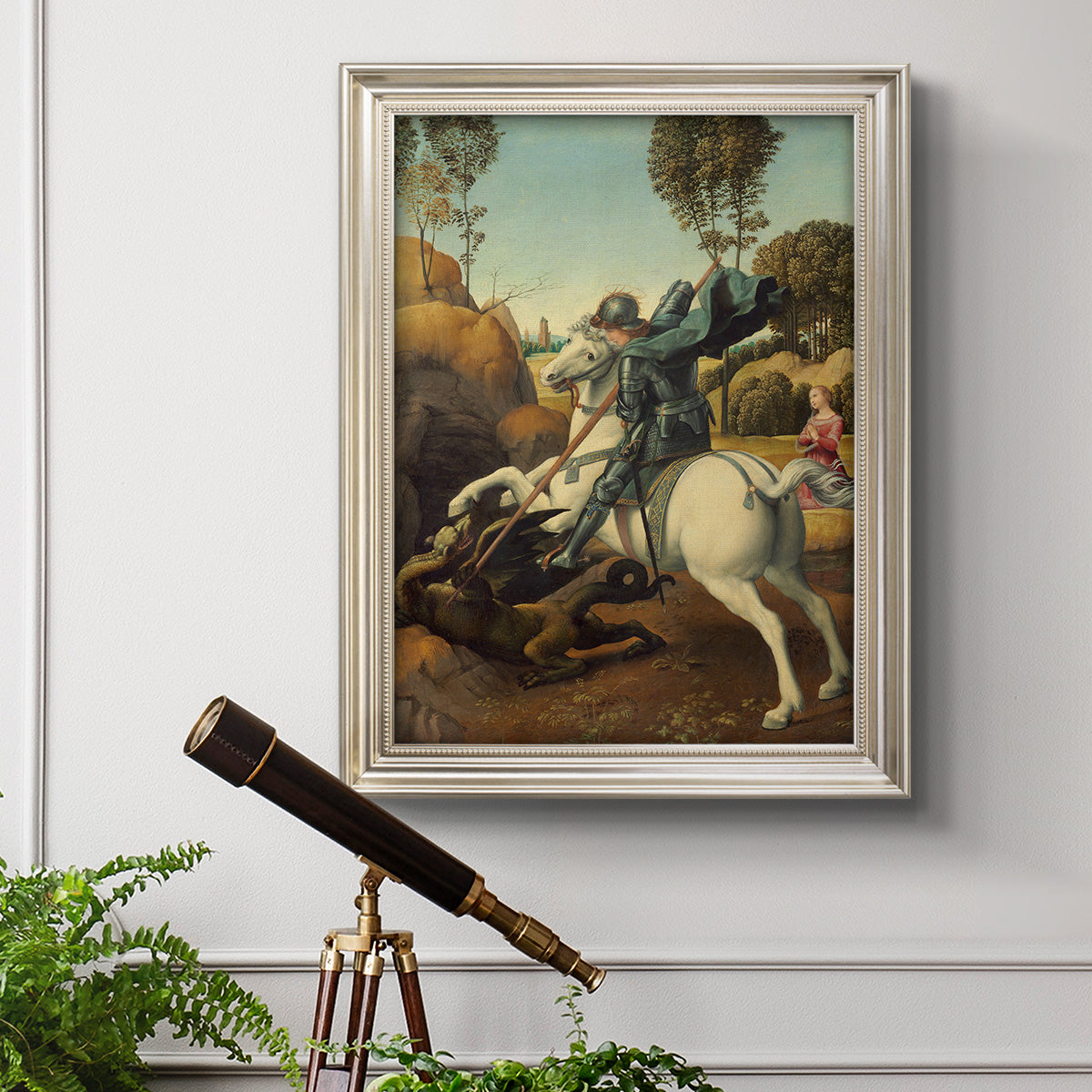 Religious painting of Saint George slaying the dragon by Raphael in an ornate champagne frame displayed in a light-toned interior setting.