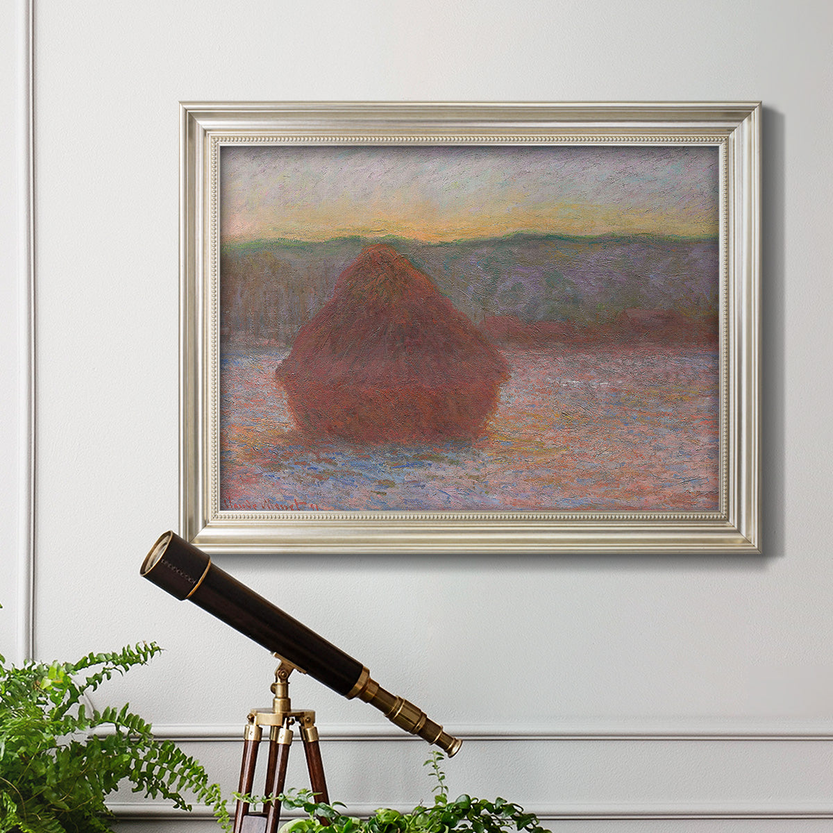 Impressionist haystack sunset scene in winter by Claude Monet in an ornate champagne frame displayed in a light-toned interior setting.