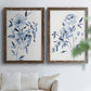 Set of two walnut barnwood framed canvas prints depicting indigo blossoms, gestural blue leaves, and airy white space arranged across two complementary compositions above a sofa in a bright living space.
