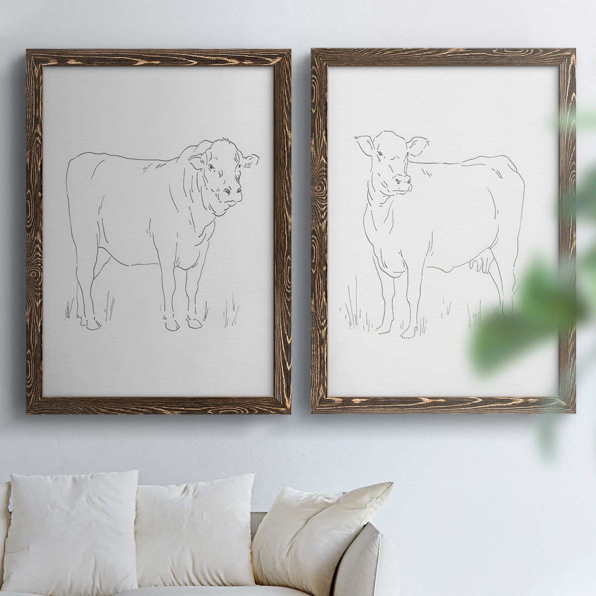 Set of two walnut barnwood framed canvas prints depicting fine gray lines, white backgrounds, and quiet farm-animal profiles arranged across two complementary compositions above a sofa in a bright living space.