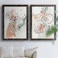 Set of two black barnwood framed canvas prints depicting scribbled petals, translucent washes, and drifting stems arranged across two complementary compositions above a sofa in a bright living space.