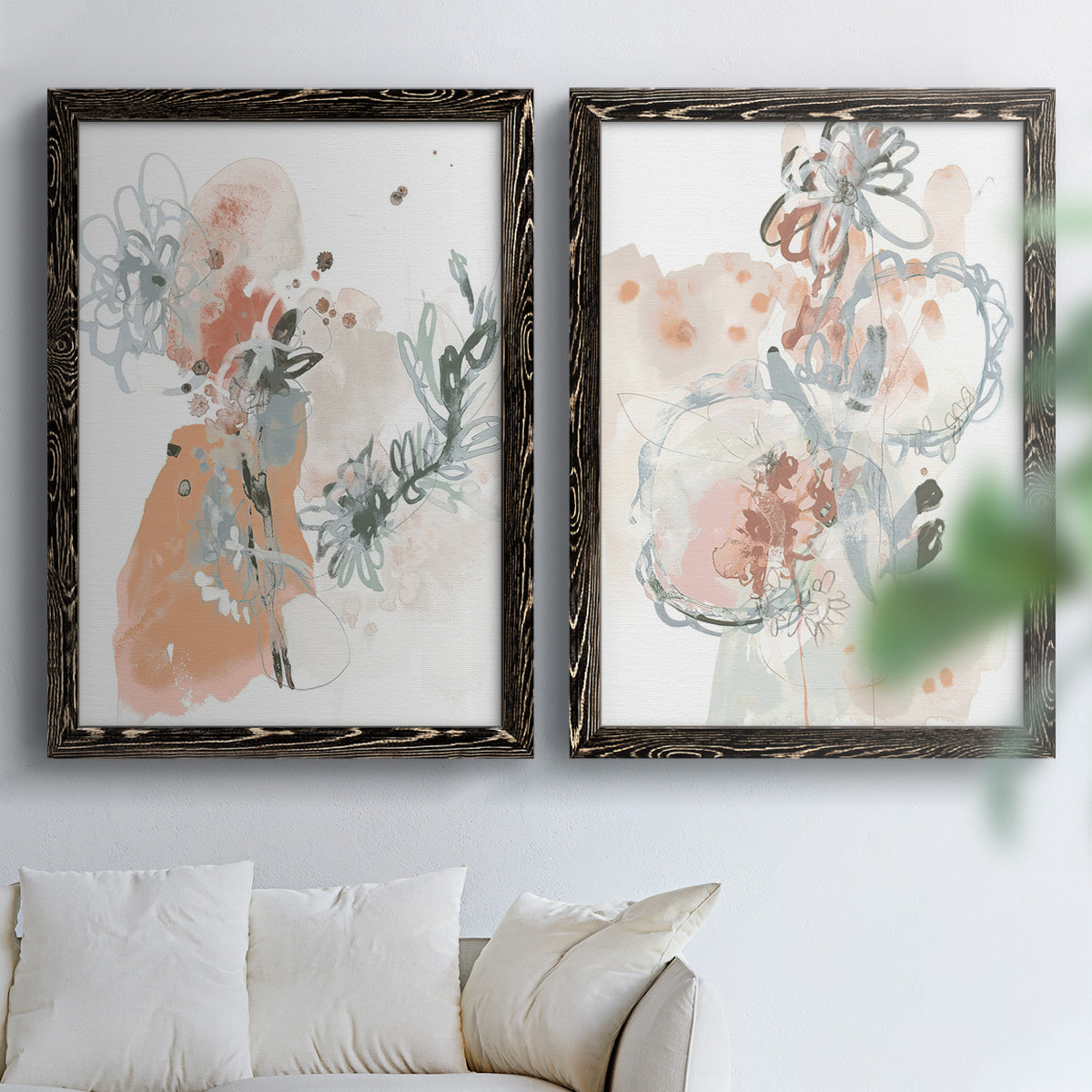 Set of two black barnwood framed canvas prints depicting scribbled petals, translucent washes, and drifting stems arranged across two complementary compositions above a sofa in a bright living space.