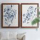 Set of two maple barnwood framed canvas prints depicting indigo blossoms, gestural blue leaves, and airy white space arranged across two complementary compositions above a sofa in a bright living space.