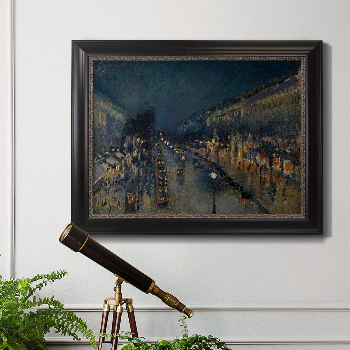 Impressionist nighttime Paris street scene by Camille Pissarro in an ornate black frame with gilded inner detail displayed in a light-toned interior setting.