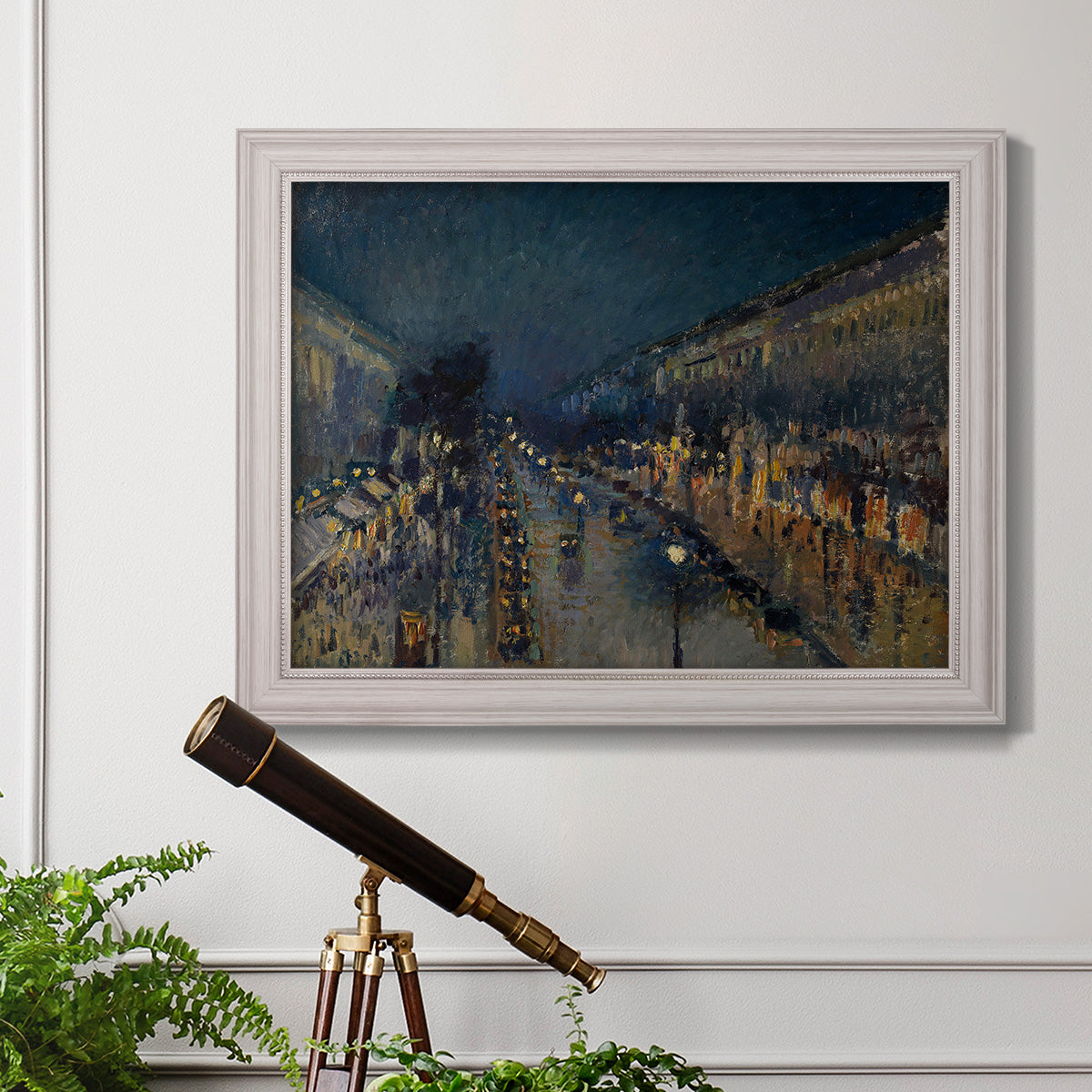 Impressionist nighttime Paris street scene by Camille Pissarro in an ornate weathered white frame displayed in a light-toned interior setting.