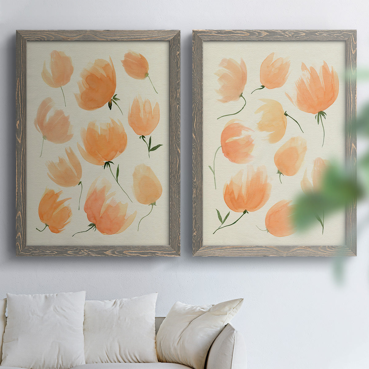 Set of two gray barnwood framed canvas prints depicting soft petals, thin black stems, and warm cream backgrounds arranged across two complementary compositions above a sofa in a bright living space.