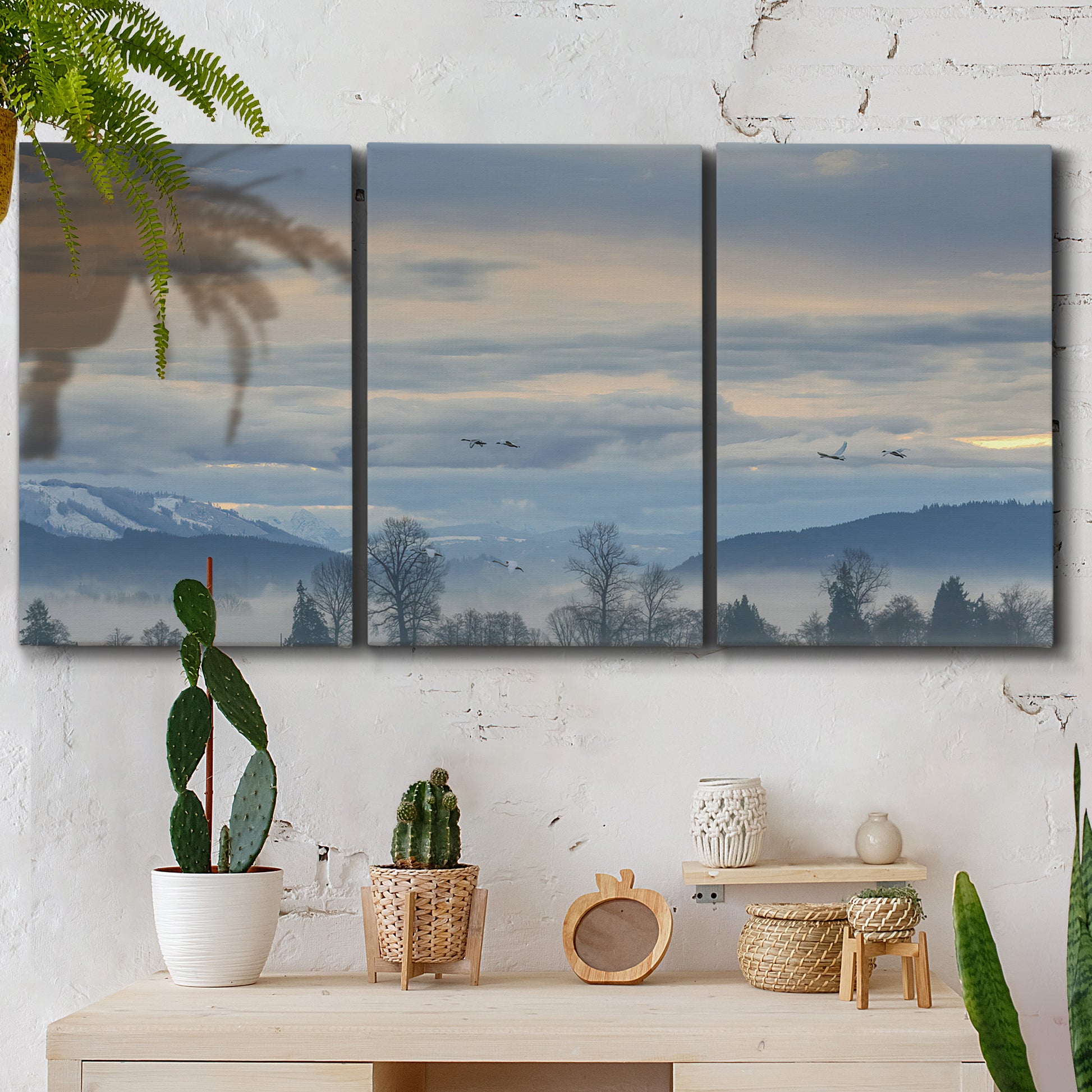 Three-panel canvas wall art featuring misty horizon over quiet landscape, displayed in a boho-chic entryway above a console table.