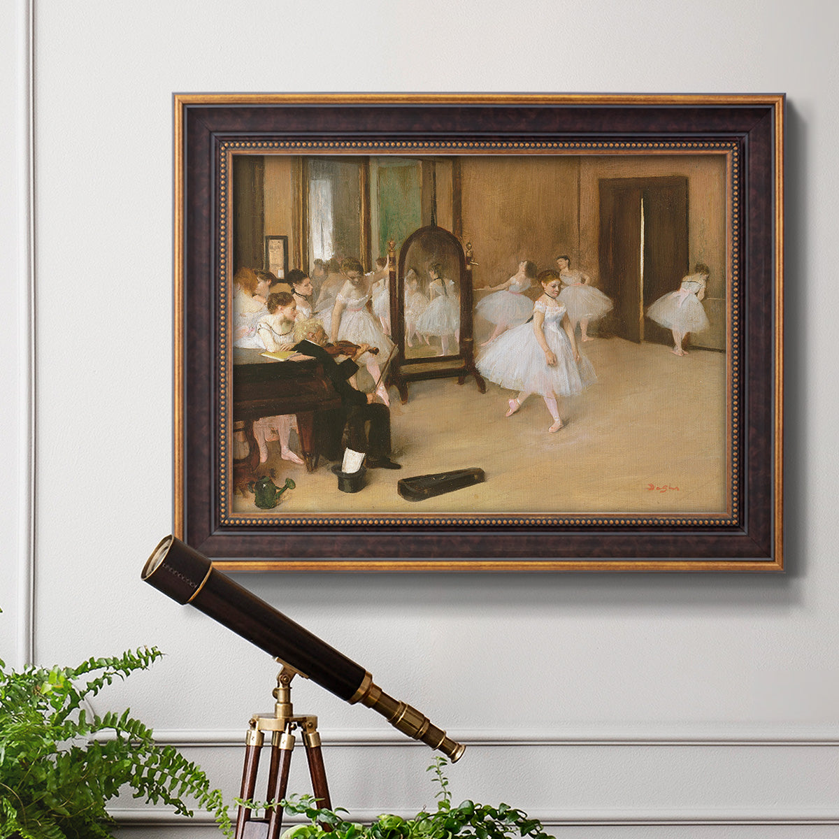 Impressionist dance class interior scene by Edgar Degas in an ornate bronzed mahogany wood frame displayed in a light-toned interior setting.