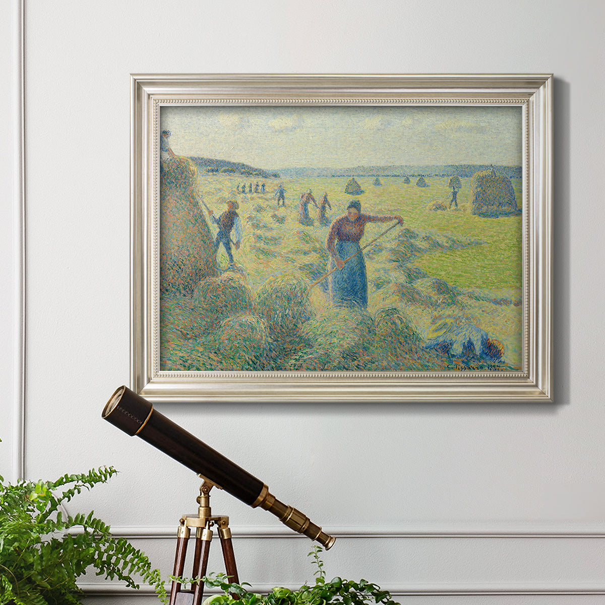 Impressionist rural hay harvest landscape by Camille Pissarro in an ornate champagne frame displayed in a light-toned interior setting.