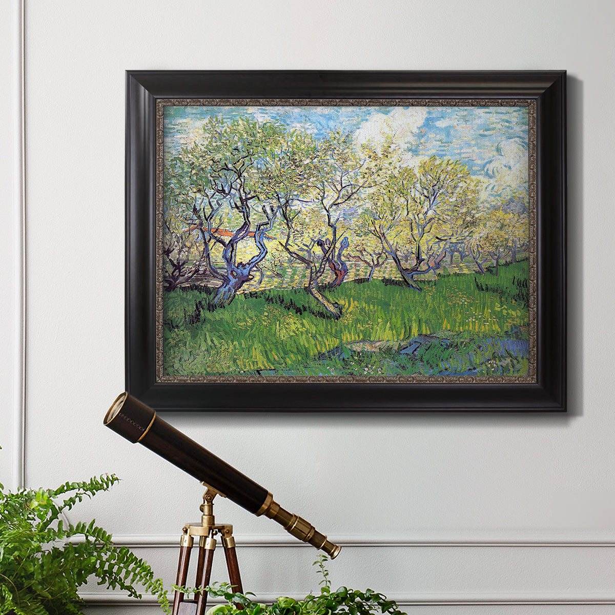 Impressionist spring orchard landscape by Vincent van Gogh in an ornate black frame with gilded inner detail displayed in a light-toned interior setting.