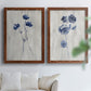 Set of two maple barnwood framed canvas prints depicting indigo blossoms, thin stems, and softly distressed gray backgrounds arranged across two complementary compositions above a sofa in a bright living space.