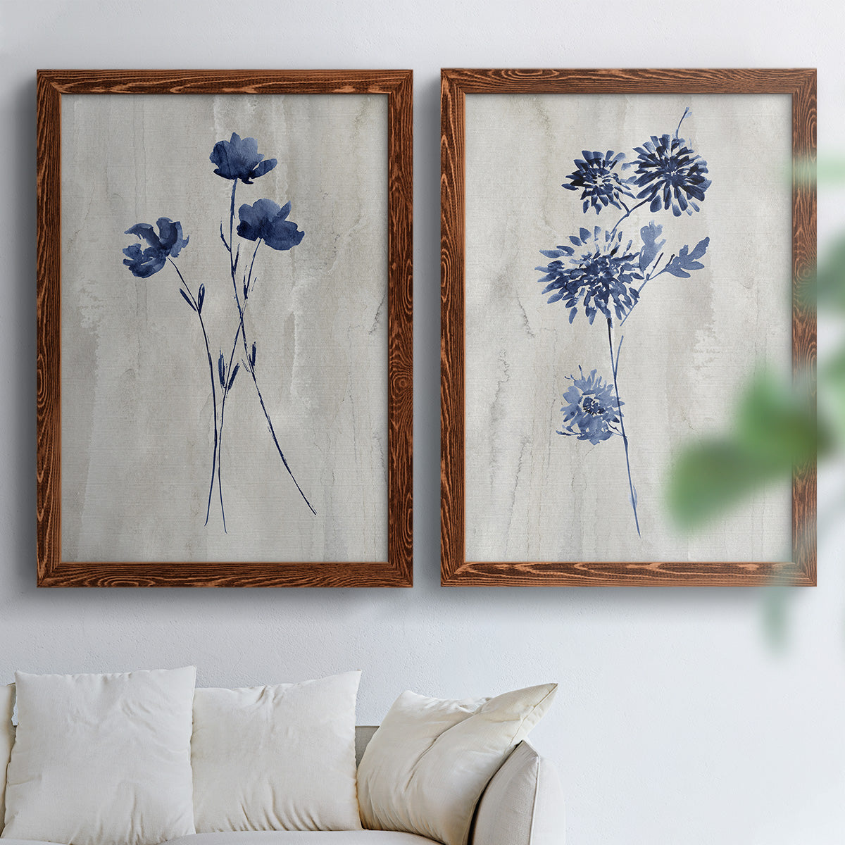 Set of two maple barnwood framed canvas prints depicting indigo blossoms, thin stems, and softly distressed gray backgrounds arranged across two complementary compositions above a sofa in a bright living space.