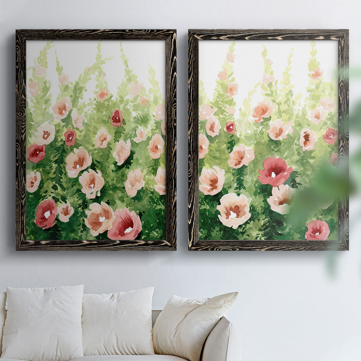 Set of two black barnwood framed canvas prints depicting loose blossoms, green stems, and sunlit watercolor texture arranged across two complementary compositions above a sofa in a bright living space.
