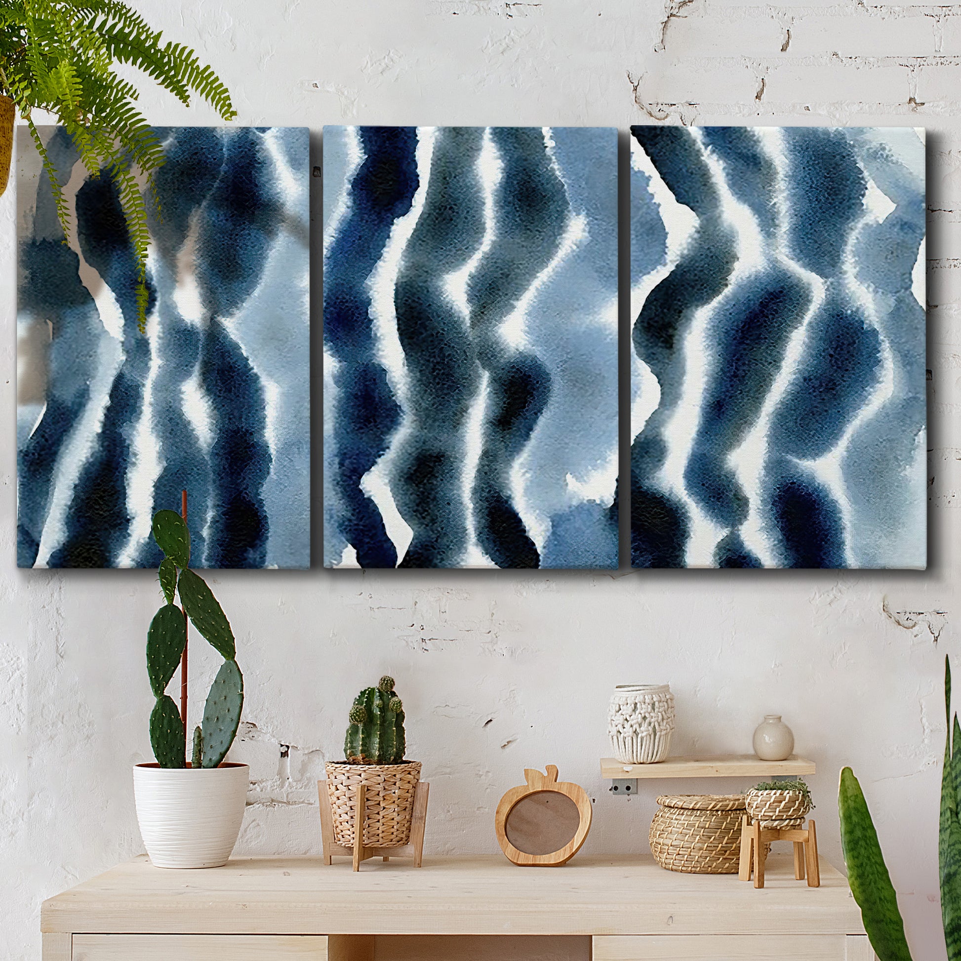 Three-panel canvas wall art featuring flowing blue watercolor wave forms, displayed in a boho-chic entryway above a console table.