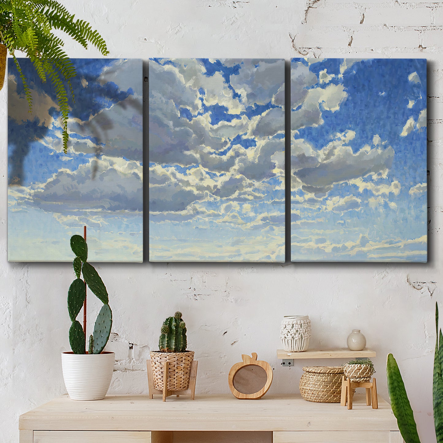 Three-panel canvas wall art featuring whimsical cloud filled sky landscape, displayed in a boho-chic entryway above a console table.