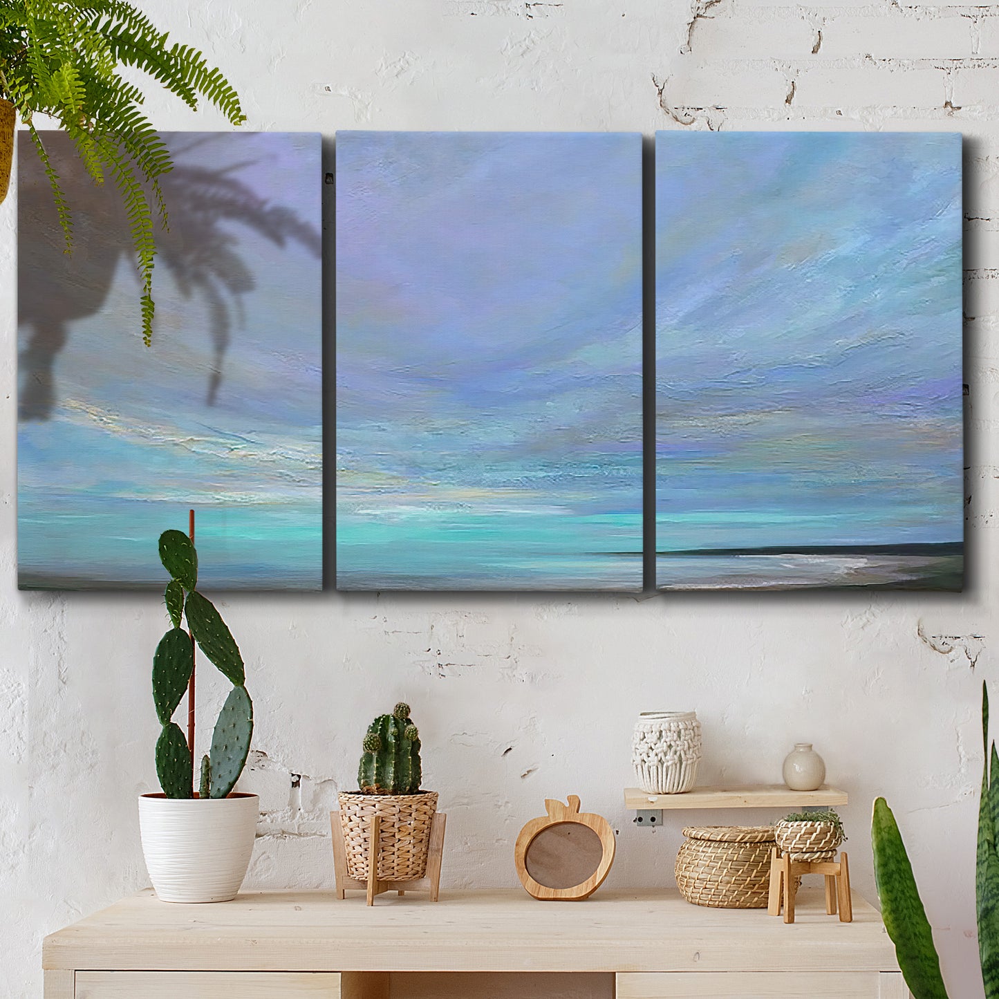 Three-panel canvas wall art featuring coastal shoreline with gentle surf, displayed in a boho-chic entryway above a console table.