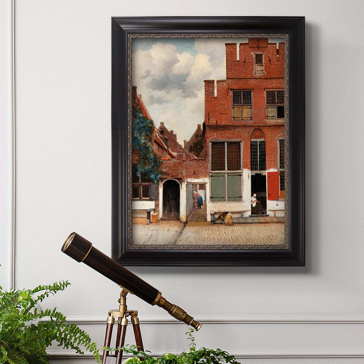 Realist city street scene by Johannes Vermeer in an ornate black frame with gilded inner detail displayed in a light-toned interior setting.