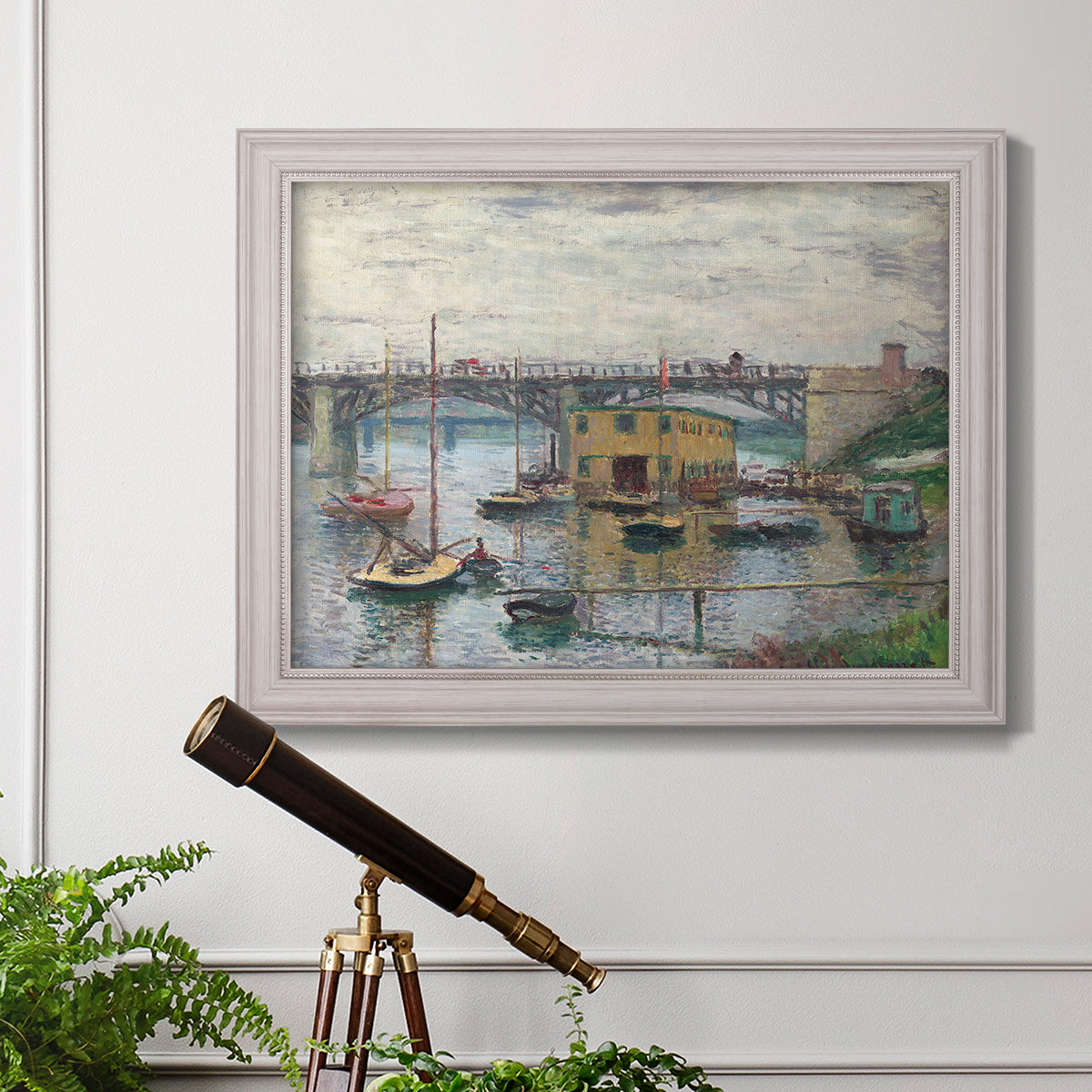 Impressionist river bridge scene on an overcast day by Claude Monet in an ornate weathered white frame displayed in a light-toned interior setting.