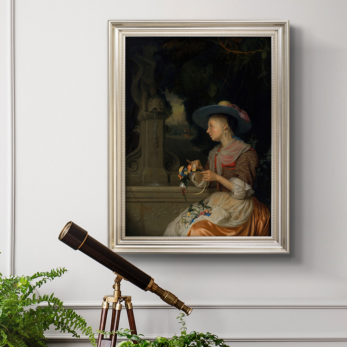 Classical interior scene of a woman weaving flowers by Godfried Schalcken in an ornate champagne frame displayed in a light-toned interior setting.