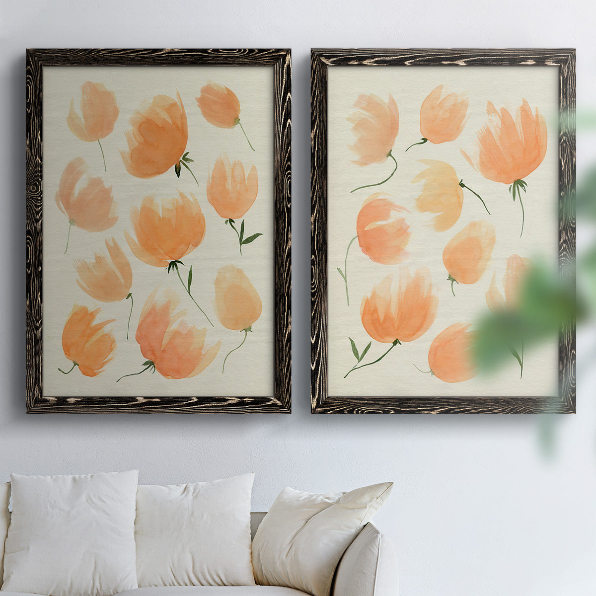 Set of two black barnwood framed canvas prints depicting soft petals, thin black stems, and warm cream backgrounds arranged across two complementary compositions above a sofa in a bright living space.