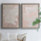 Set of two gray barnwood framed canvas prints depicting cloudy rose washes, broad pale strokes, and subtle texture arranged across two complementary compositions above a sofa in a bright living space.