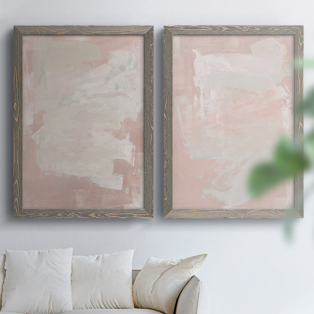 Set of two gray barnwood framed canvas prints depicting cloudy rose washes, broad pale strokes, and subtle texture arranged across two complementary compositions above a sofa in a bright living space.