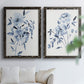 Set of two black barnwood framed canvas prints depicting indigo blossoms, gestural blue leaves, and airy white space arranged across two complementary compositions above a sofa in a bright living space.
