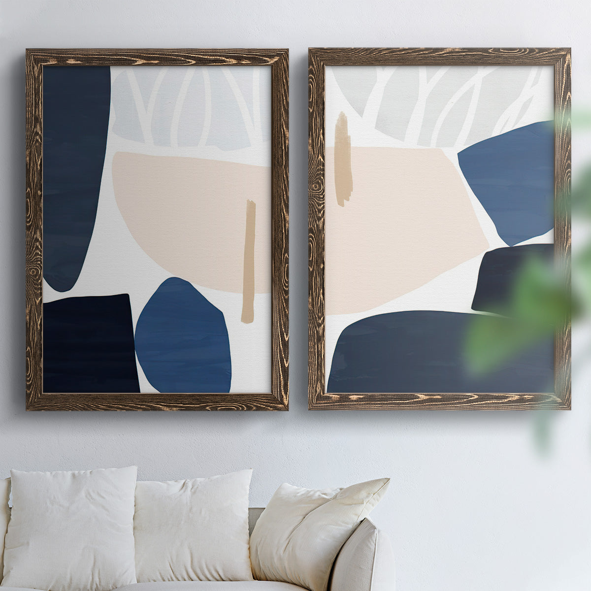 Set of two walnut barnwood framed canvas prints depicting rounded dark forms, pale sand fields, and clean modern edges arranged across two complementary compositions above a sofa in a bright living space.