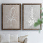 Set of two walnut barnwood framed canvas prints depicting delicate stems, leaves, and blossoms against gray taupe and pale blue panels arranged across two complementary compositions above a sofa in a bright living space.