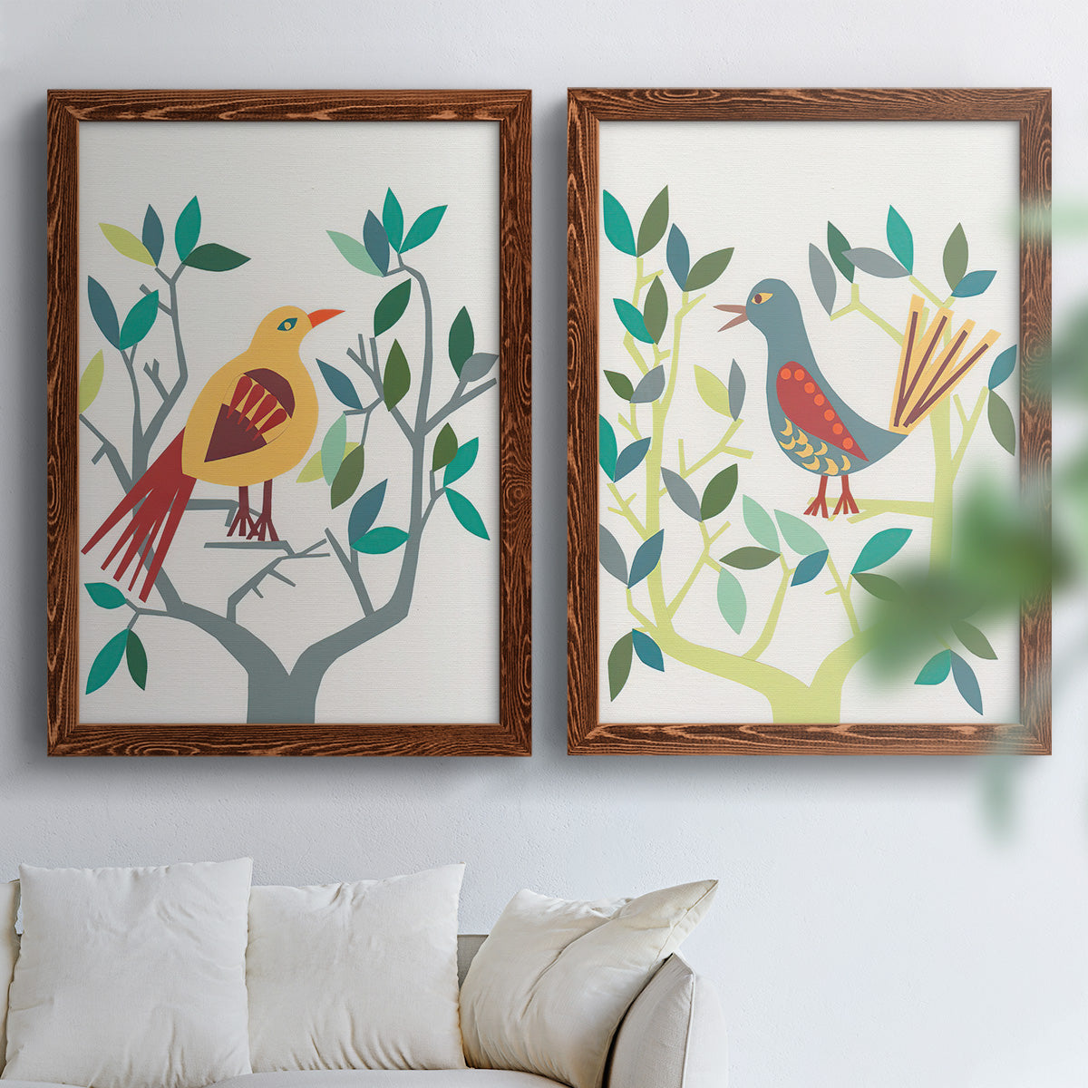 Set of two maple barnwood framed canvas prints depicting red yellow blue plumage, simplified leaves, and playful flat shapes arranged across two complementary compositions above a sofa in a bright living space.