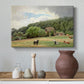 Canvas art print featuring a rural landscape with cows feeding on grass near buildings, styled above a decorative console