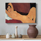 Canvas art print featuring a stylized female nude with elongated proportions resting on couch, styled above a decorative console