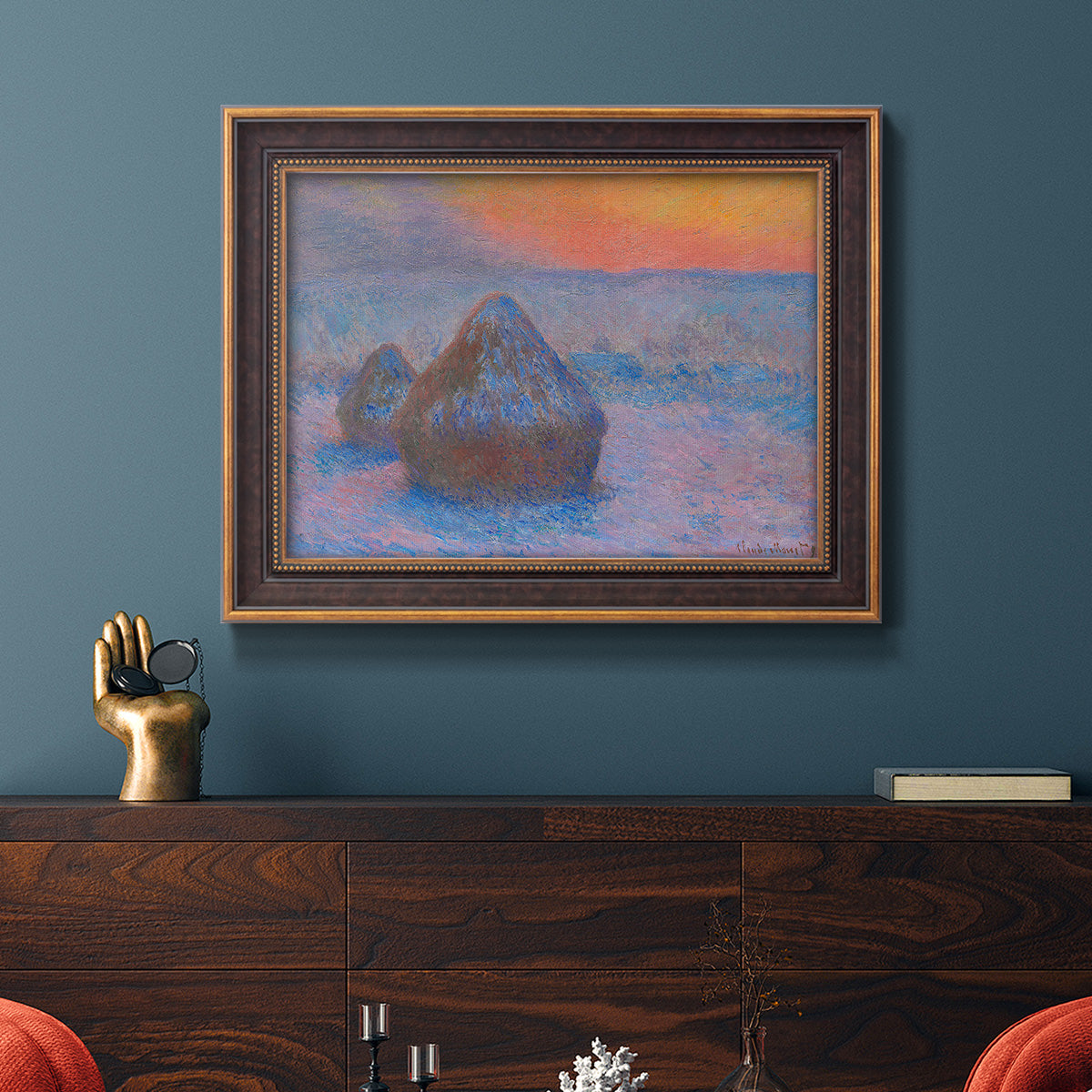 Impressionist haystack scene at sunset by Claude Monet in an ornate bronzed mahogany wood frame displayed in a dark-toned interior setting.