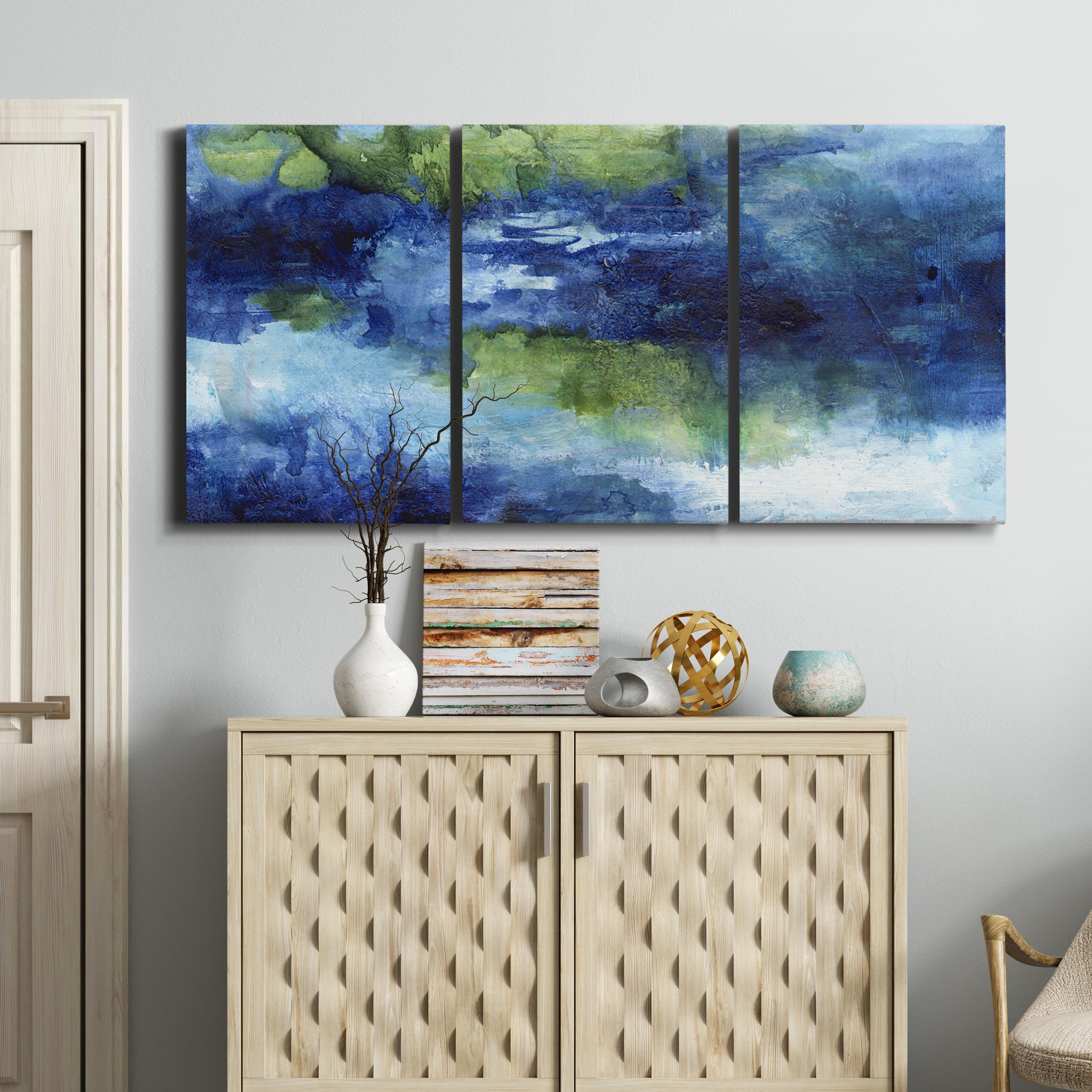 Three-panel canvas wall art featuring flowing blue abstract watercolor, displayed above a cabinet in an entryway.