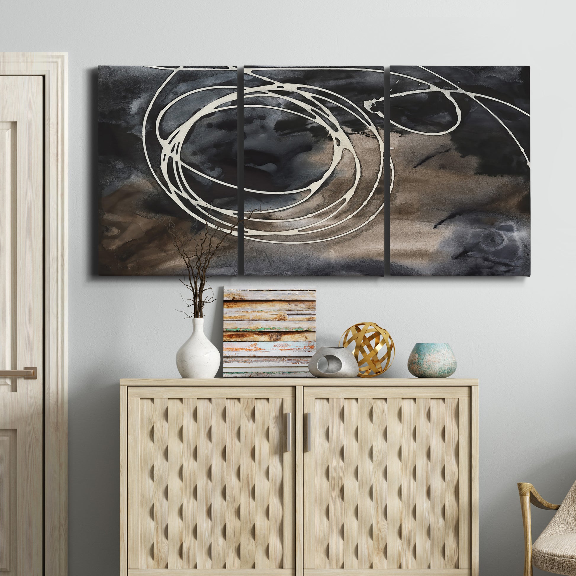 Three-panel canvas wall art featuring dark swirling abstract motion, displayed above a cabinet in an entryway.