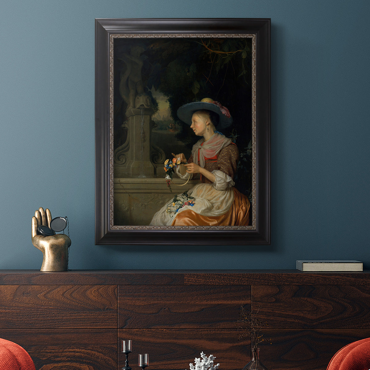 Classical interior scene of a woman weaving flowers by Godfried Schalcken in an ornate black frame with gilded inner detail displayed in a dark-toned interior setting.