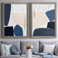 Set of two gray barnwood framed canvas prints depicting paired minimalist color-block abstracts with rounded dark forms, pale sand fields, and clean modern edges above a sofa in a contemporary living room.