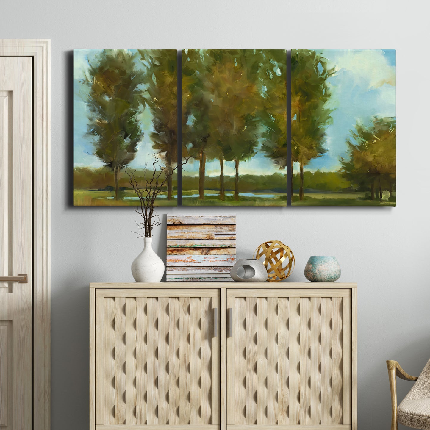 Three-panel canvas wall art featuring tall trees lining open landscape, displayed above a cabinet in an entryway.