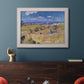 Impressionist wheat harvest scene by Vincent van Gogh in an ornate weathered white frame displayed in a dark-toned interior setting.