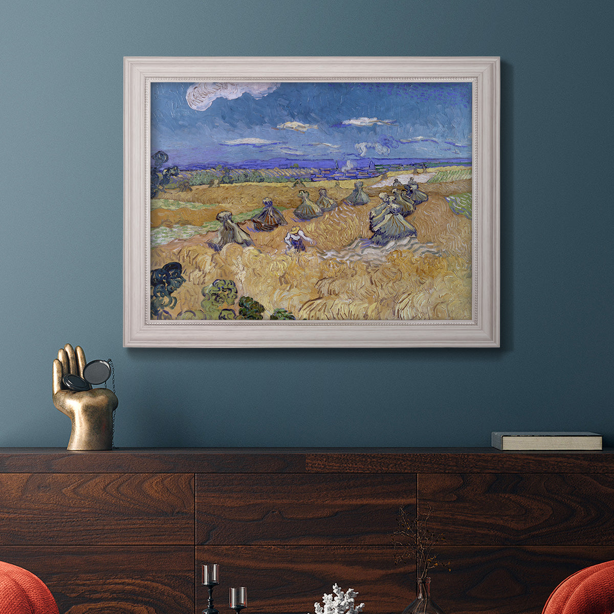 Impressionist wheat harvest scene by Vincent van Gogh in an ornate weathered white frame displayed in a dark-toned interior setting.
